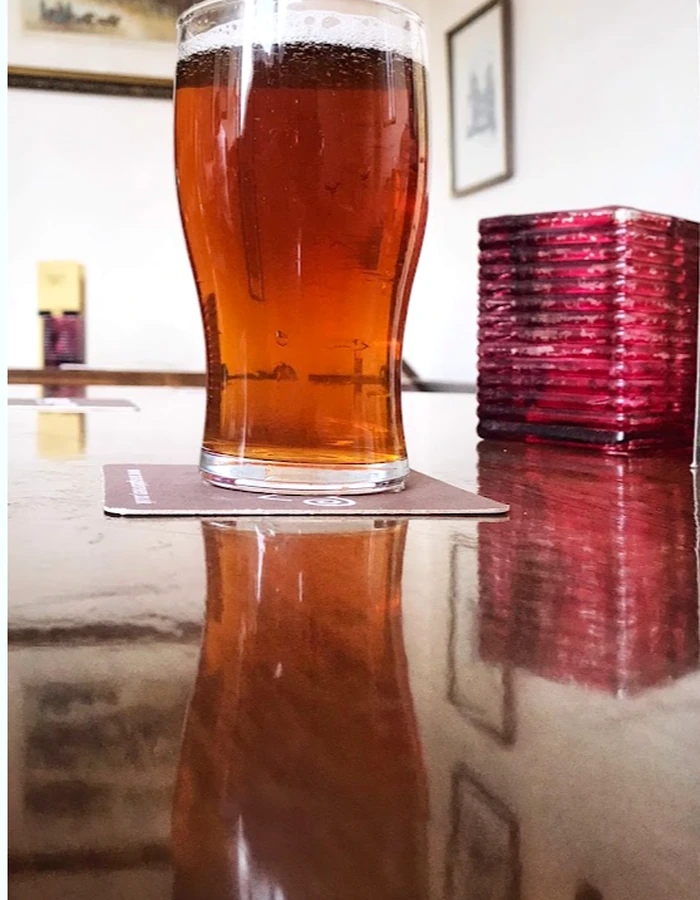 A pint of amber beer beside a red glass candle holder